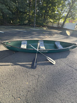 Green Sun Dolphin canoe & paddles, parked on asphalt. Enhance your outdoor adventure with an RV rental!