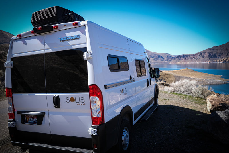 White Winnebago Solis Pocket camper van, ideal for rv rental, parked by a scenic lake with mountains under a blue sky. — photo 7