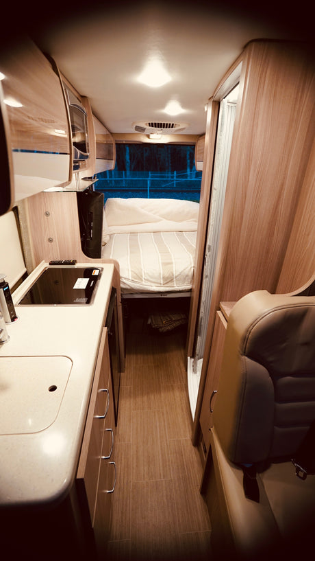 Inside a well-lit RV rental: modern kitchen with sink/stovetop, comfortable bed, and seating area for your travels.