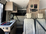 Inside a modern RV rental: light wood cabinets, white quilted seats, kitchen, and system controls.