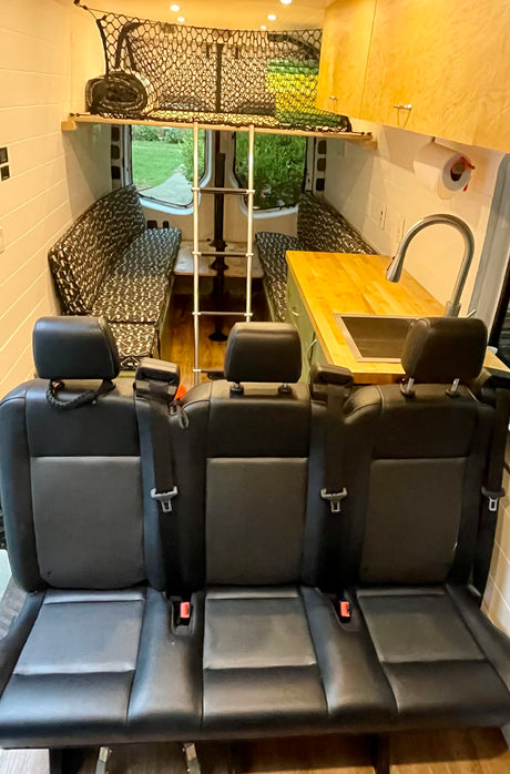RV rental interior: three black seats, a compact kitchen with sink, cozy bench seating, and overhead storage net, ready for adventure.