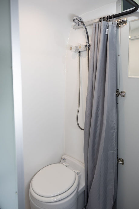 Compact RV rental bathroom featuring a toilet, shower, and gray curtain, ideal for travel convenience.