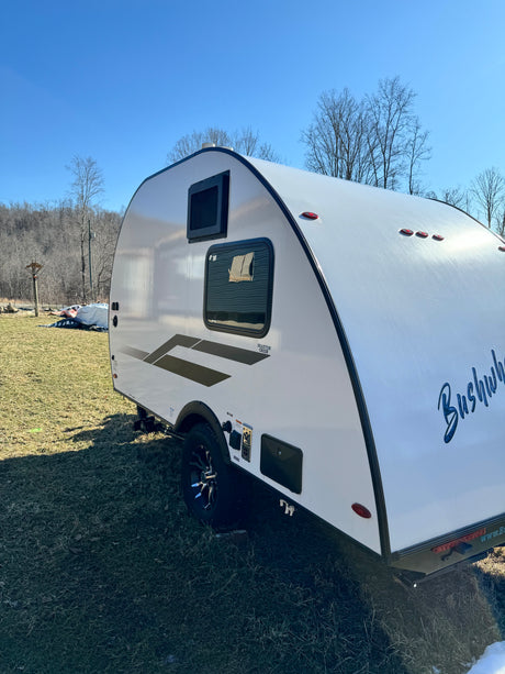 Compact white Braxton Creek Bushwhacker teardrop RV rental on grass under blue sky, ready for outdoor adventures.