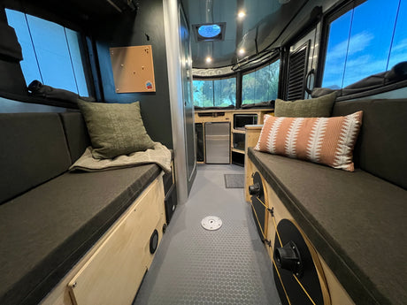 RV rental interior: cozy bench seating, compact kitchen, and large windows with blue sky views. Perfect for your next adventure.
