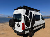 Explore the outdoors with this white RV rental camper van, featuring custom graphics, parked on a sandy beach near the water.