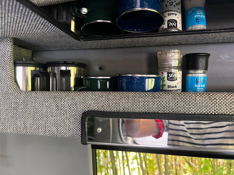 Neatly organized kitchen supplies, including mugs & spice grinders, in an RV rental for road trips and camping.