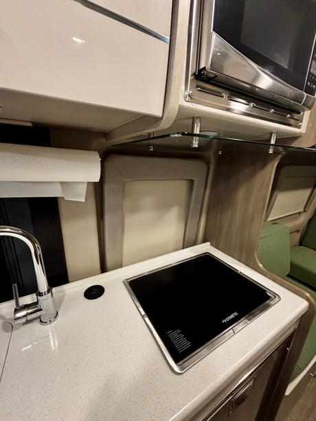 Modern rv rental kitchen with a Dometic induction cooktop, faucet, and microwave. Speckled countertop & paper towels.