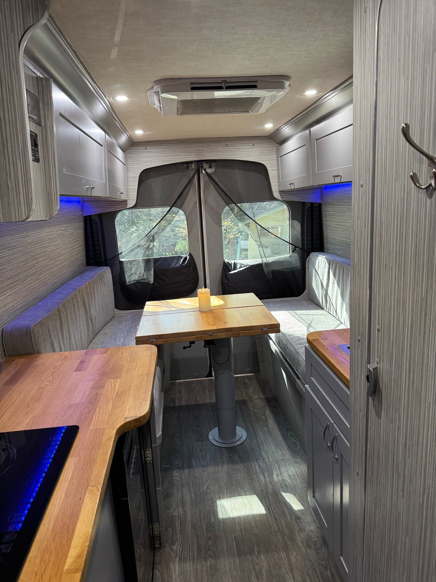 and a striking patterned blanket on the bed.|Experience tranquil moments in this RV rental's dinette. A candle on the wooden table overlooks a scenic nature view through the screen.|Relax in an RV rental! Comfy bed with a blue and white blanket — photo 6