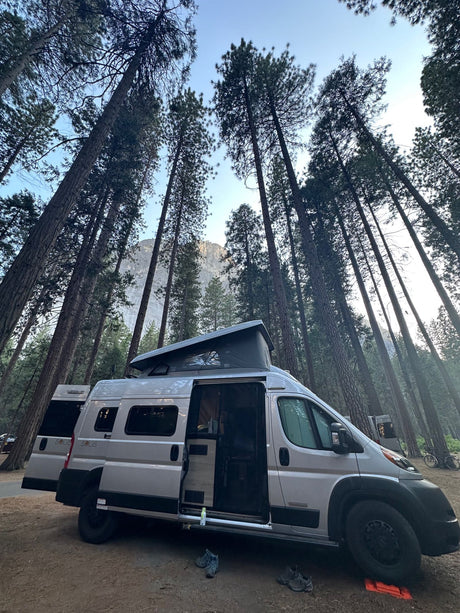 RV rental van parked in a serene tall pine forest with a mountain vista. Pop-top raised for camping.