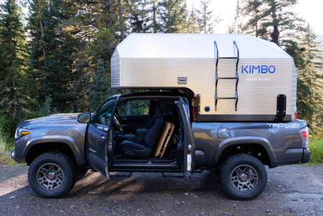 Gray Toyota Tacoma with a Kimbo truck camper attached, ideal for an RV rental outdoor adventure or camping trip.