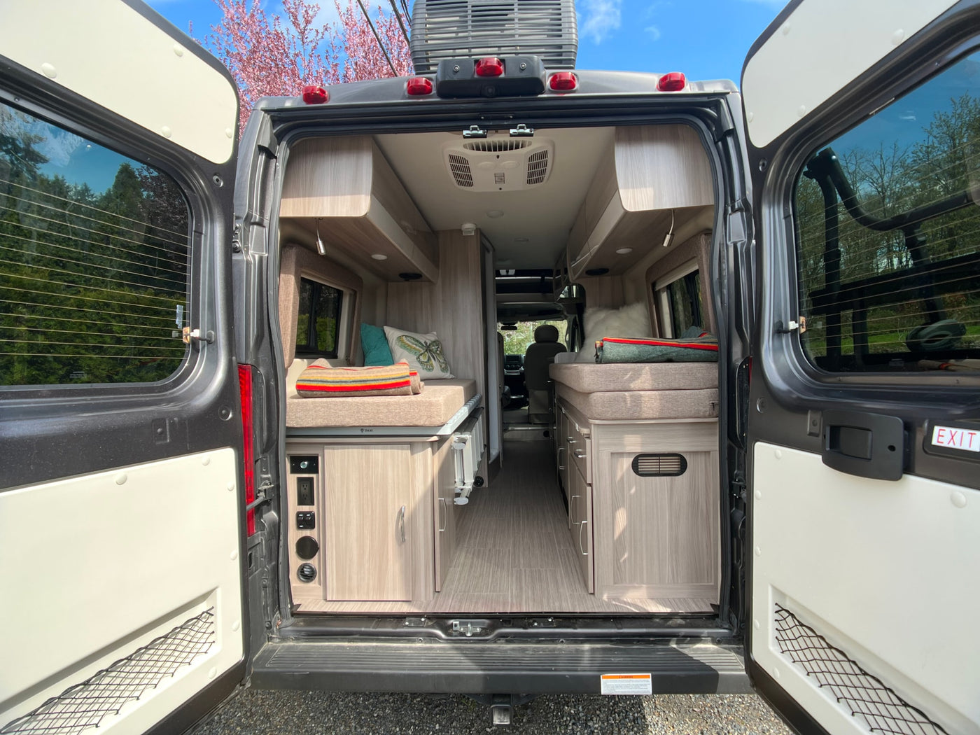 Open rear doors of an **rv rental** camper van reveal its cozy interior with bed areas, storage cabinets, and a clean floor. — photo 8