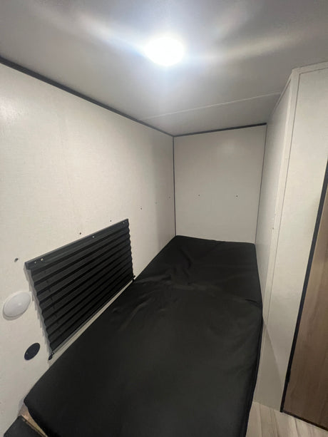 RV rental sleeping area featuring a black bed, wall shade, and bright overhead light, creating a compact space.