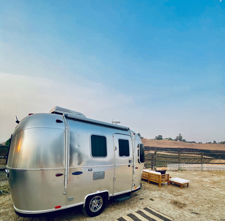 Experience nature: a silver Airstream RV rental parked with an outdoor seating area in a scenic, rural landscape.