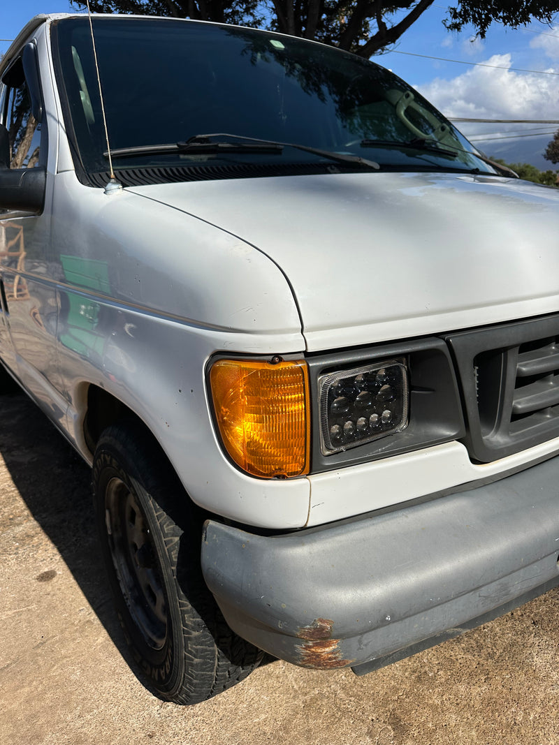 White van (potential RV rental) front right: amber turn signal, LED headlight, gray bumper with rust, antenna. Parked on concrete. — photo 4