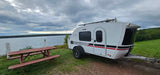 Enjoy nature with this Luna Rover teardrop camper, perfect for RV rental, overlooking a scenic lake with a picnic table.