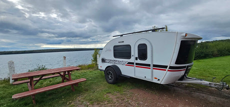 Enjoy nature with this Luna Rover teardrop camper, perfect for RV rental, overlooking a scenic lake with a picnic table.