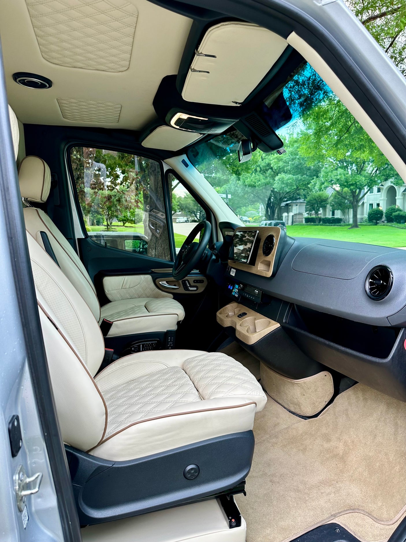 Luxurious rv rental interior: cream quilted seats, wood-look dash, and a clear view through the front windshield.