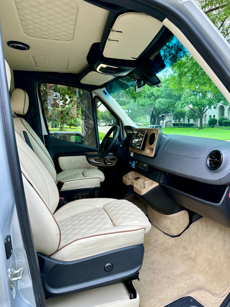 Luxurious rv rental interior: cream quilted seats, wood-look dash, and a clear view through the front windshield.