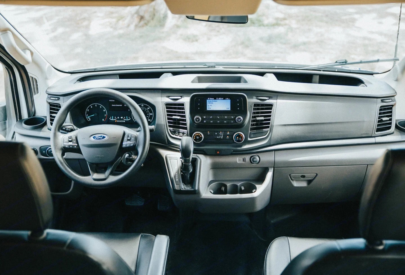 This photo shows the front interior of a modern Ford Transit RV rental, featuring the dashboard, steering wheel, and central display.