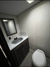Compact RV rental bathroom with a modern vanity, sink, mirror, and toilet. Features gray tile floor and textured walls, perfect for travel.