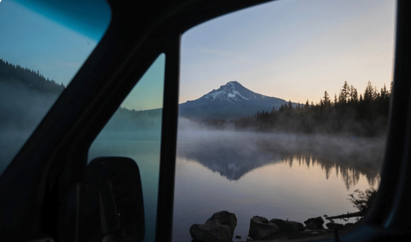 Your RV rental view: a serene lake with misty reflections of a snow-capped mountain at dawn.