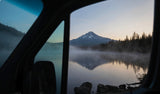 Your RV rental view: a serene lake with misty reflections of a snow-capped mountain at dawn.