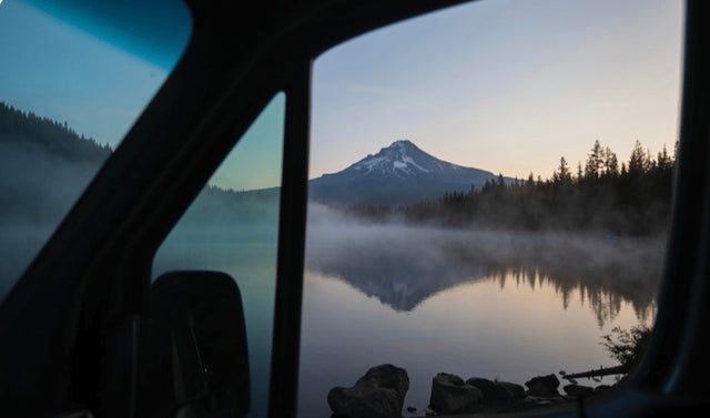 Your RV rental view: a serene lake with misty reflections of a snow-capped mountain at dawn.