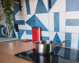 RV rental kitchen featuring a stainless saucepan on an induction stove, wood counter, and geometric blue/white tile backsplash.