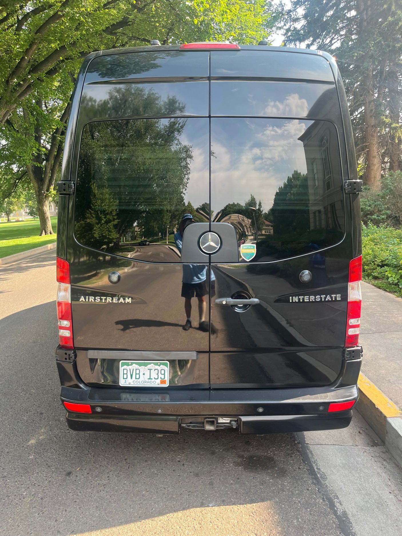 Black Airstream Interstate RV rental, with Colorado plate BVB-I39, reflecting trees & buildings from the rear.