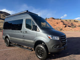 Gray Mercedes Sprinter camper van, equipped for off-road RV rental adventures, parked amidst stunning red rock scenery.