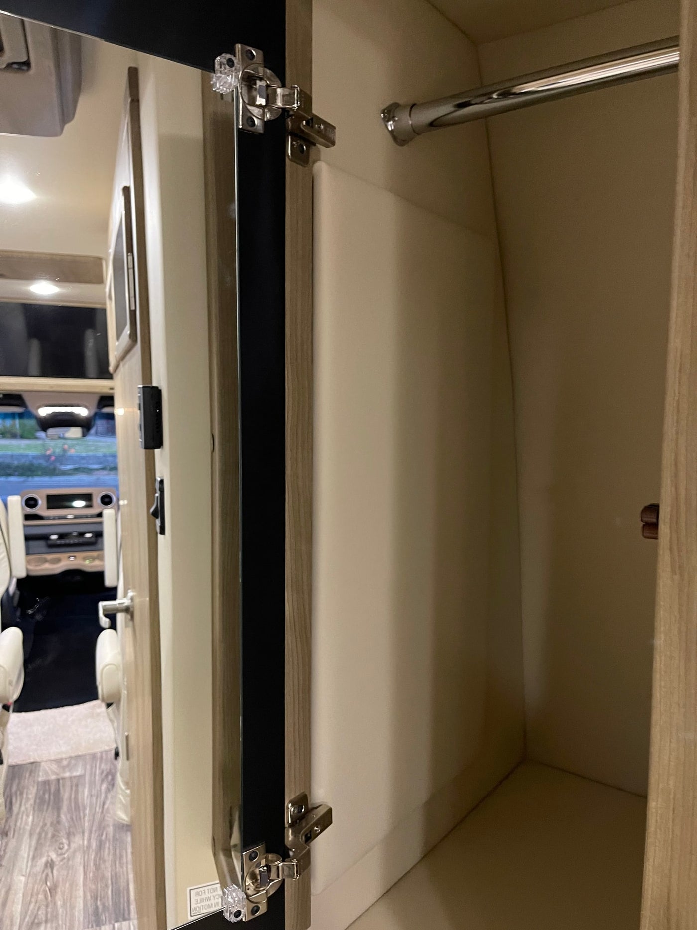 Inside an RV rental: a compact closet with a chrome hanging bar, offering storage. View into the vehicle's front cabin. — photo 13