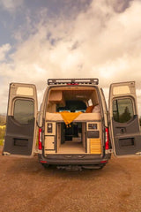 Ready for adventure? This RV rental offers a peek into a custom camper van's open rear, revealing a comfy bed & functional interior.