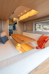 Experience an RV rental! Modern camper van interior with a bright dinette, comfy benches, and natural light from exterior views.