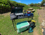 Essential camping gear for your RV rental: propane stove, cookware, cooler, and dive equipment set up outdoors.
