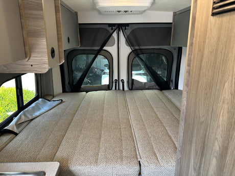 Inside this RV rental, a comfy modular bed fills the rear, with screened doors offering outdoor views.