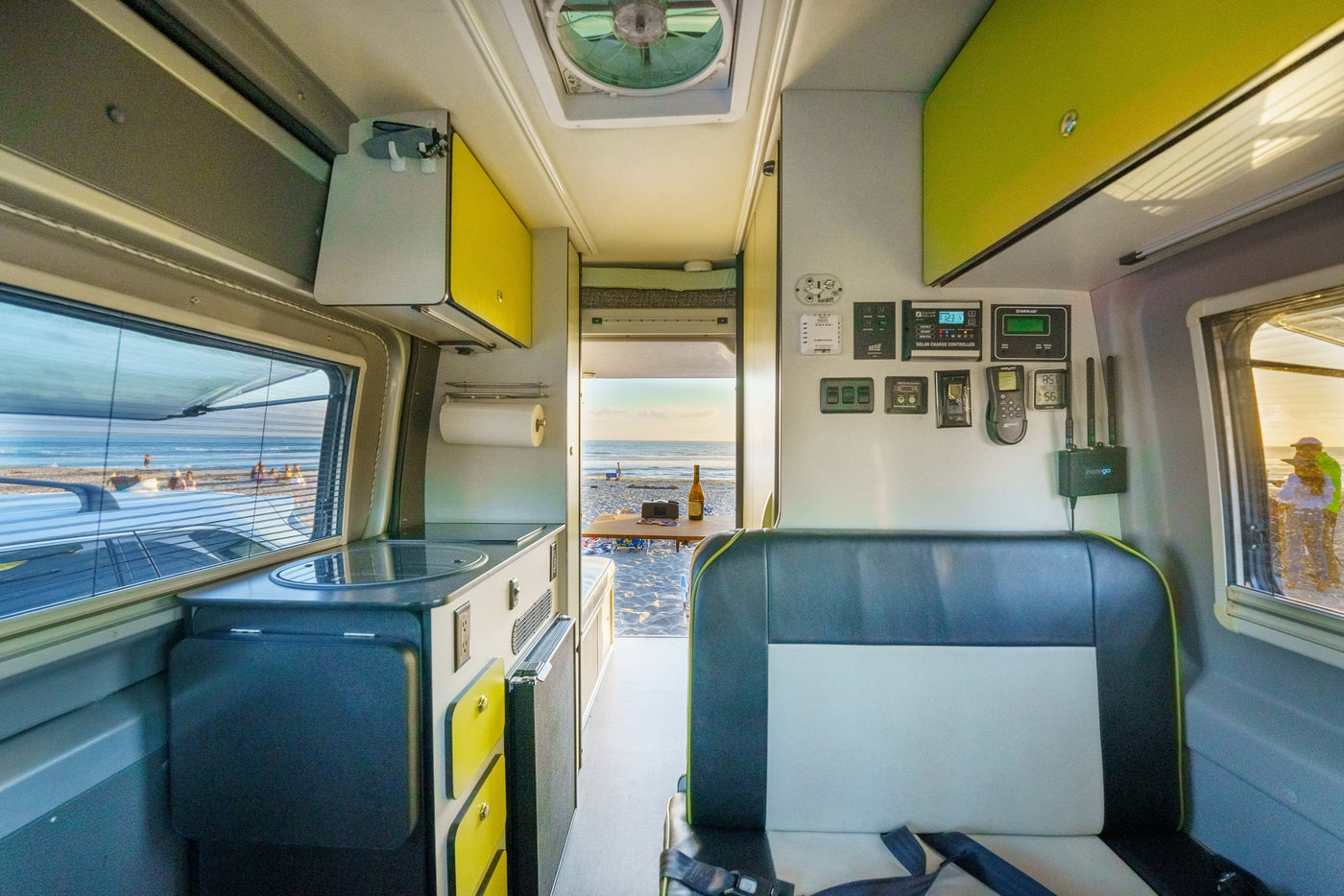 Coastal rv rental: Inside a camper van, showing kitchen, tech controls, and seating, with open doors to a lively beach. — photo 17