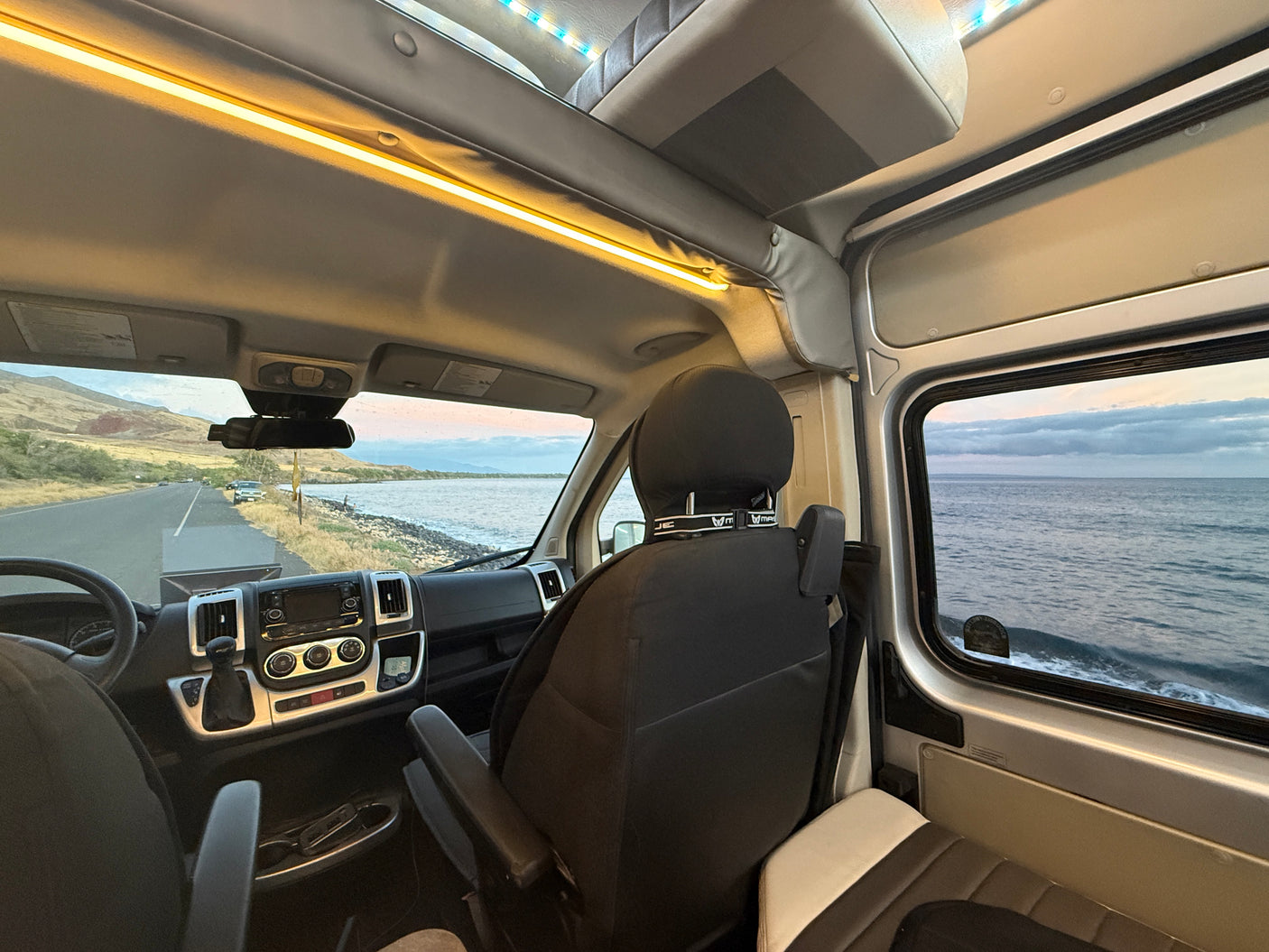 Inside a comfy RV rental, gazing at a beautiful ocean coastline and road winding by mountains. Your next travel escape!