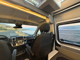 Inside a comfy RV rental, gazing at a beautiful ocean coastline and road winding by mountains. Your next travel escape!