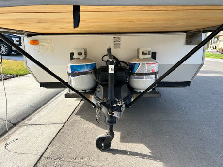 Front view of an RV rental showing its hitch, dual propane tanks, and jack stand, ready for towing.