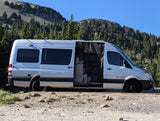 Silver rv rental camper van parked on a mountain gravel road. Side door open, showing interior, ready for adventure.