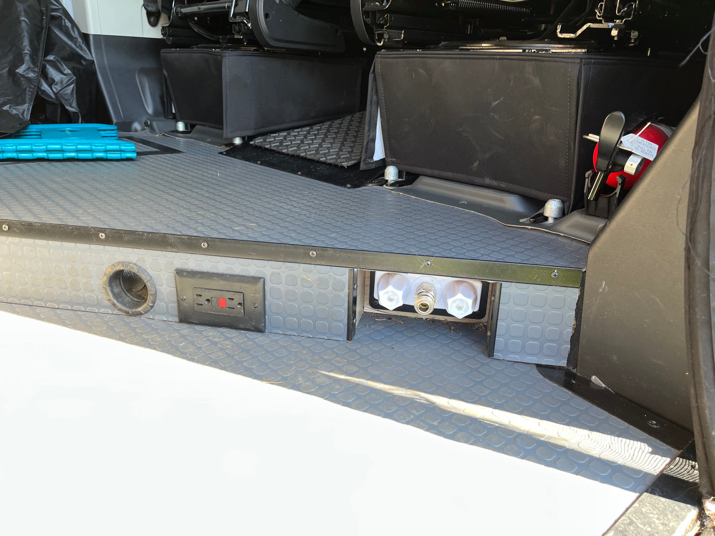 RV rental interior with grey textured floor, electrical outlet, water hookup, and fire extinguisher for safety.