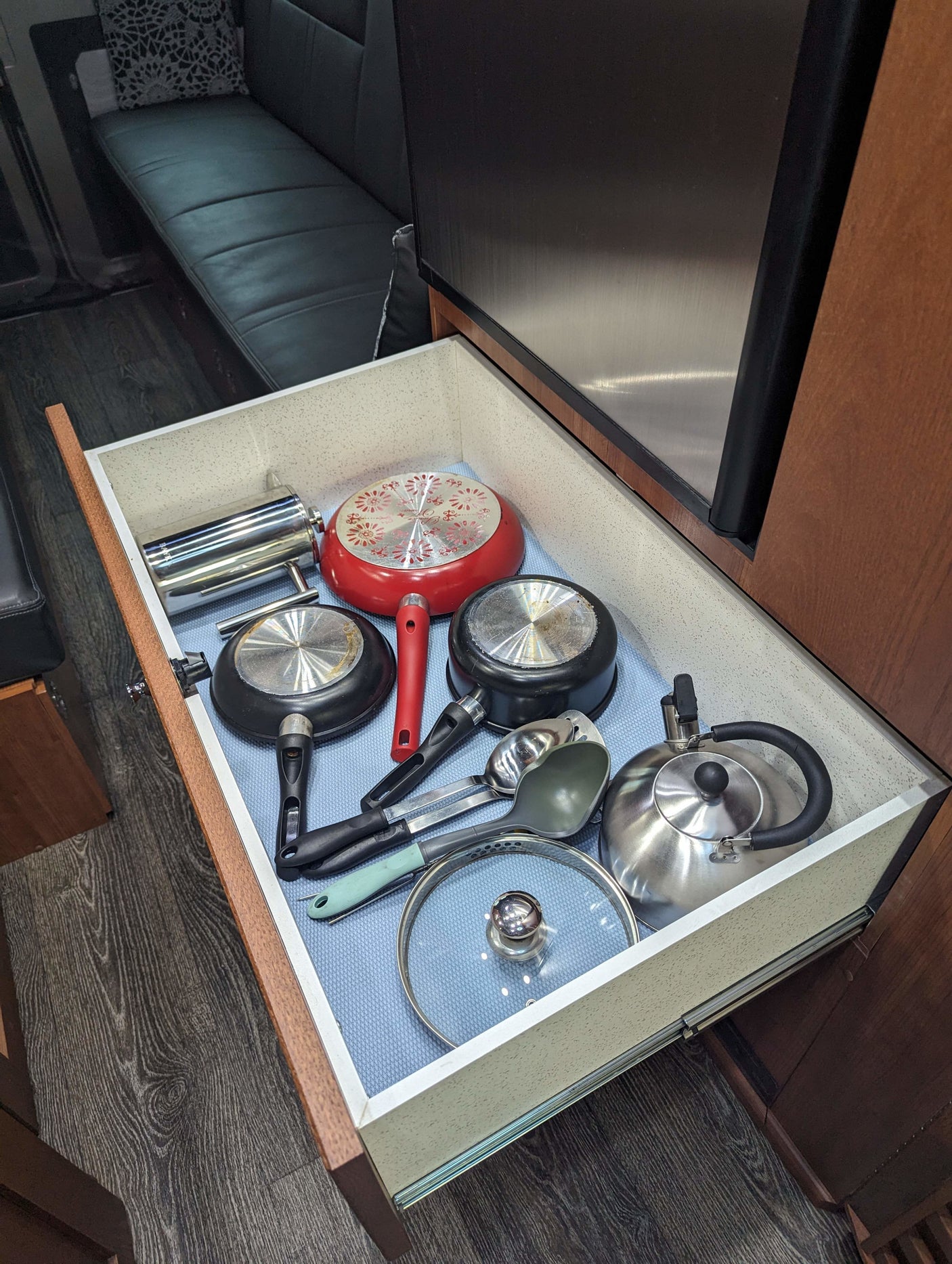 Compact RV rental kitchen drawer, neatly organized with pots, pans, a kettle, and utensils.