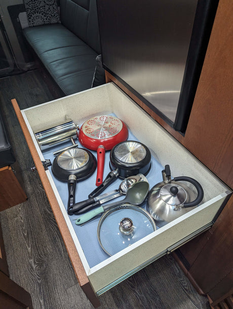 Compact RV rental kitchen drawer, neatly organized with pots, pans, a kettle, and utensils.