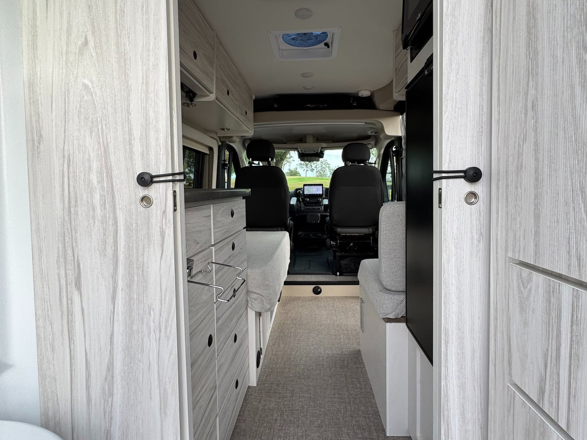  parked outside on a gravel lot under a cloudy sky.|This dark grey Entegra Coach ARC RV rental features utility hookups and a rooftop AC unit.|RV rental with a black mesh screen on the sliding door — photo 10