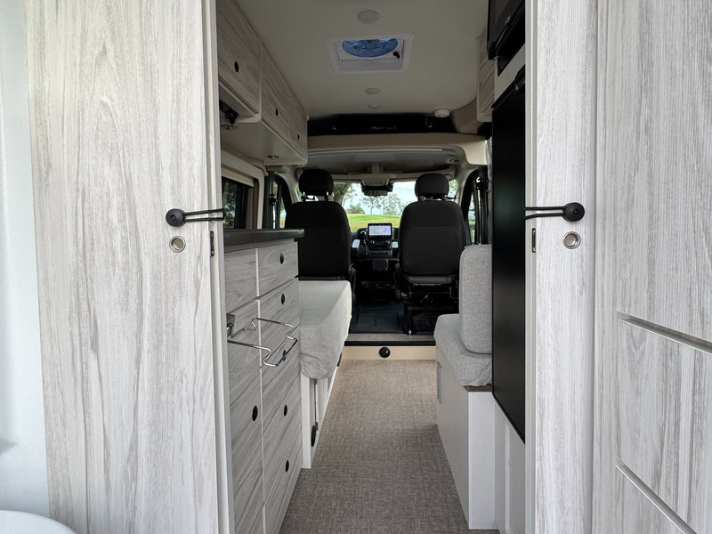  parked outside on a gravel lot under a cloudy sky.|This dark grey Entegra Coach ARC RV rental features utility hookups and a rooftop AC unit.|RV rental with a black mesh screen on the sliding door — photo 10