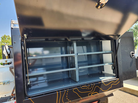 RV rental adventure ready: Open side compartment of a black camper with organized gray shelves & visible propane tank.