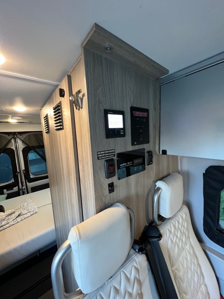 RV rental: Interior showing control panel, two light-colored seats, and a bed. Essential camper systems visible. — photo 14