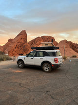 White Bronco Sport with rooftop tent parked among red rocks at sunset. Great for an RV rental adventure!