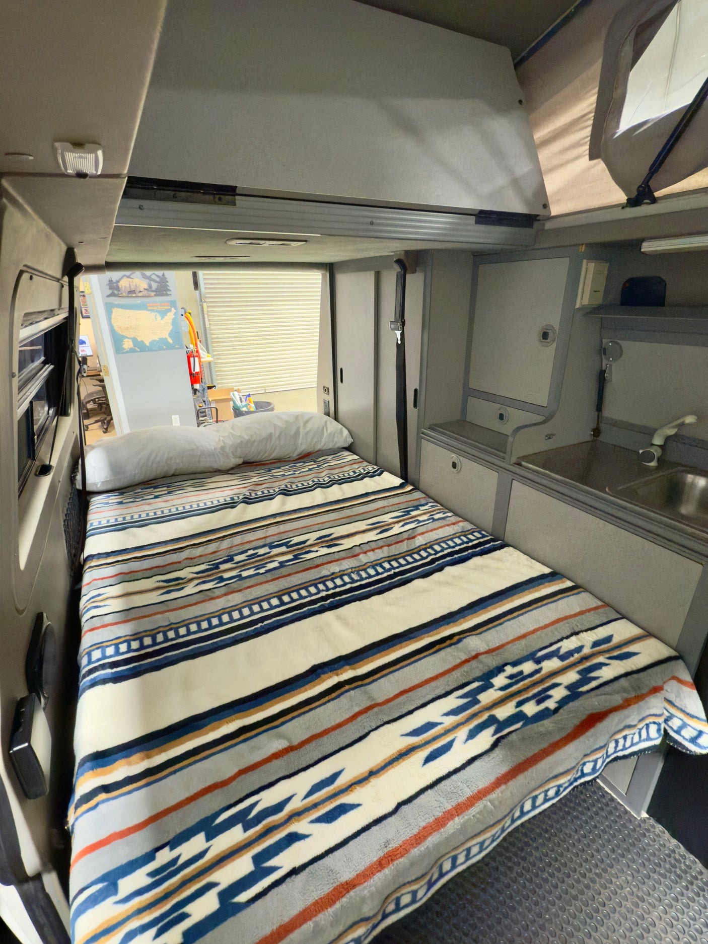 Cozy RV rental interior showcasing a patterned bed, compact kitchen with sink, and storage for adventures.