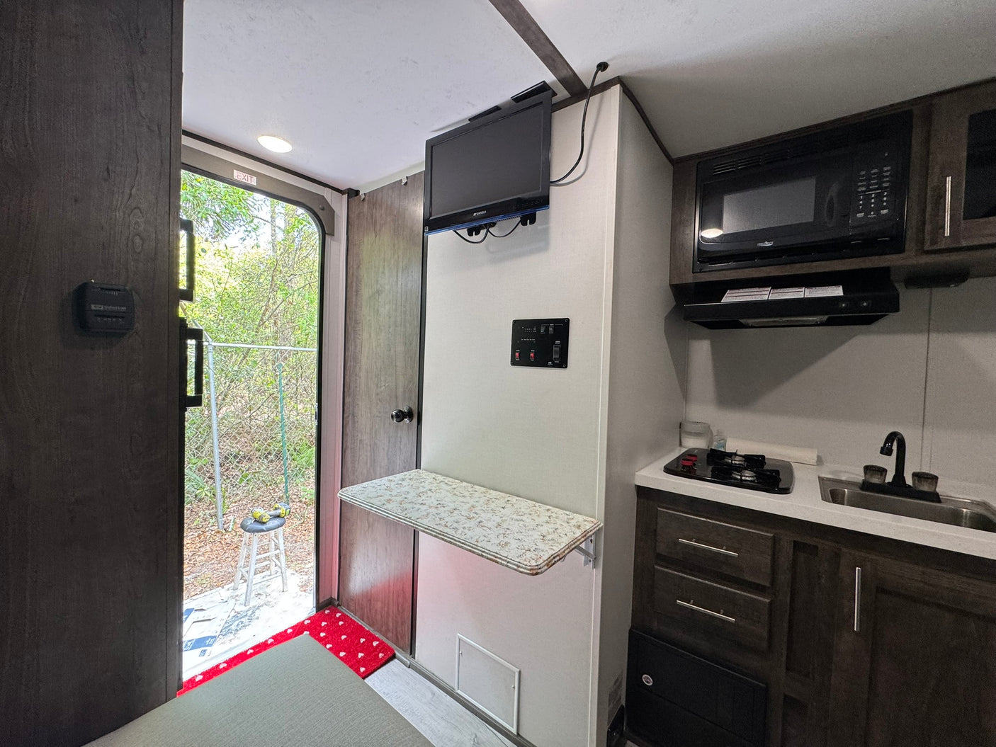Explore this compact RV rental's interior, featuring a small kitchen with microwave, sink, stovetop, and a fold-down table.